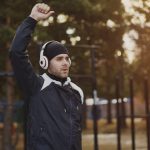 Handsome man in headphones doing stretching exercise while listening music in winter park outdoors